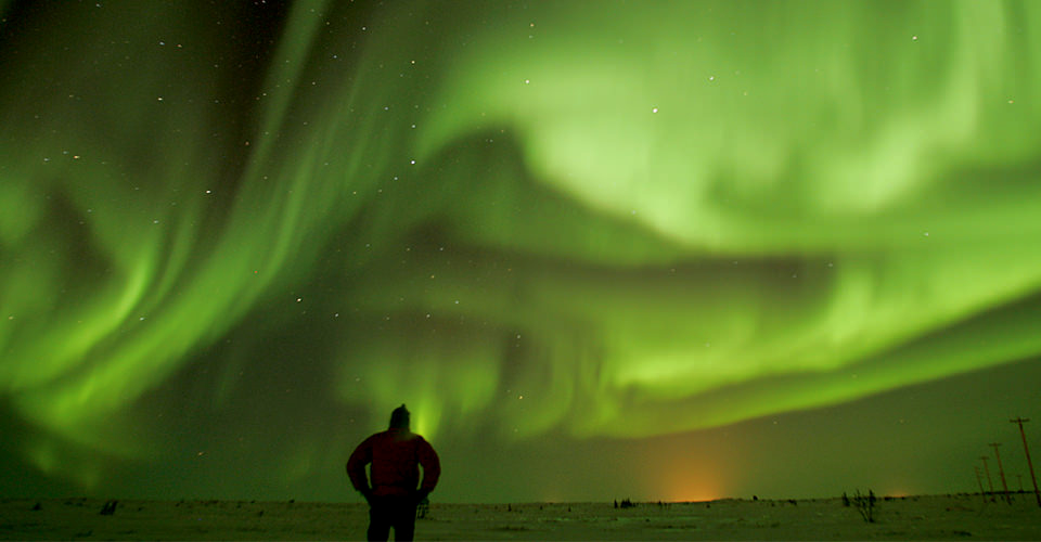 a single person is silhouetted in front of an incredible aurora display