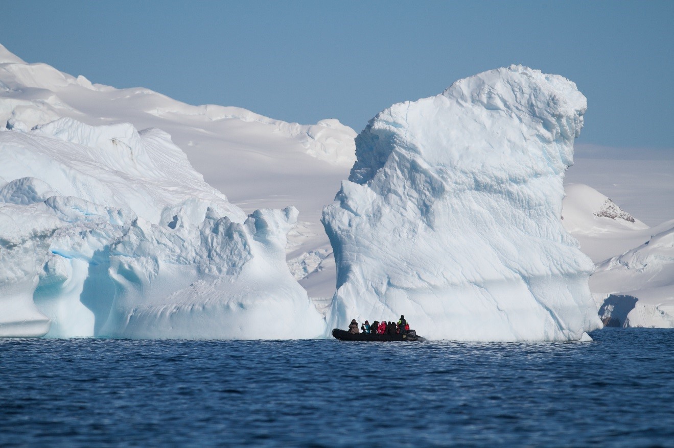 a zodiac floats along a large iceberg in Antarctica