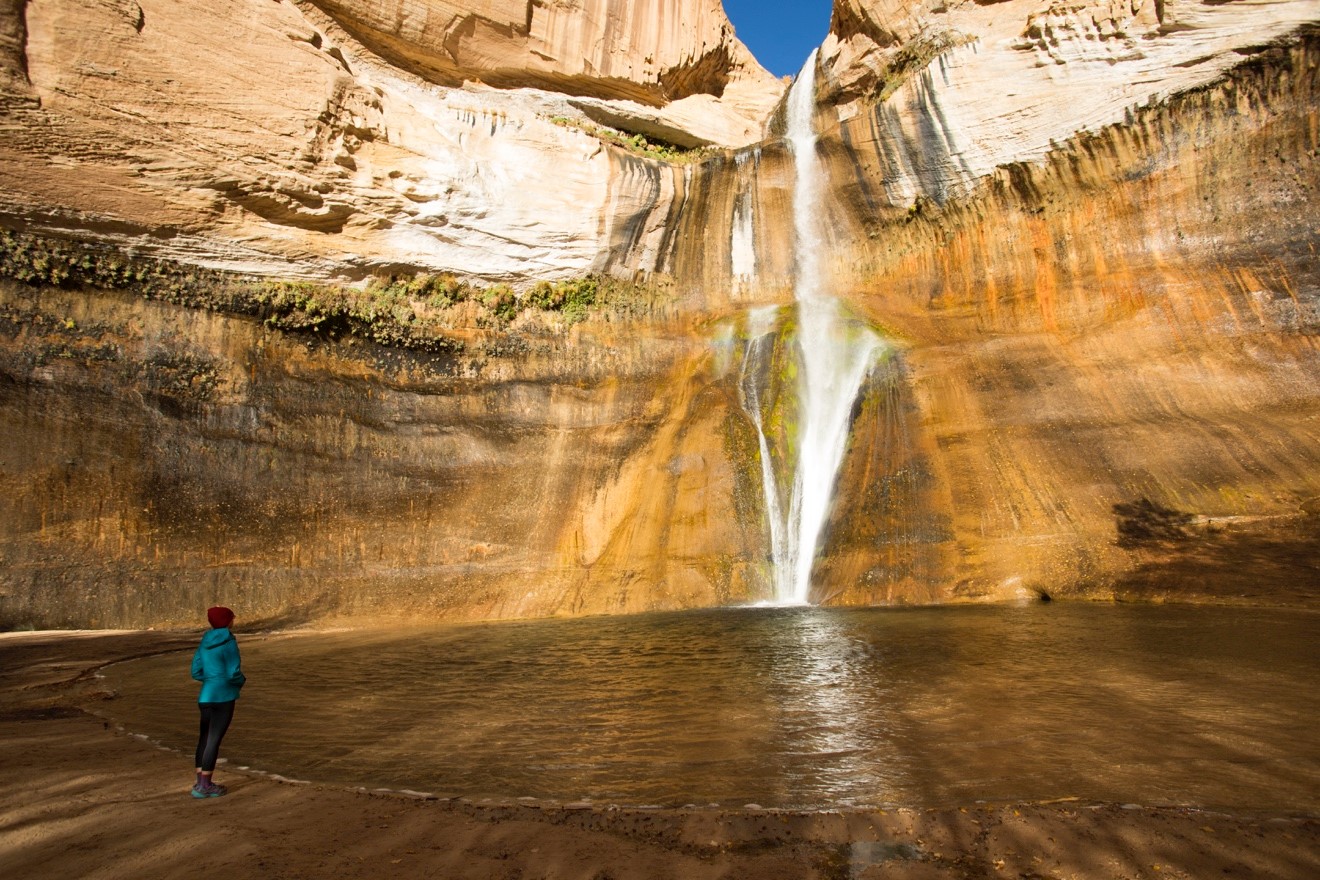 a woman peers at the majestic calf creek falls in Escalante National Monument
