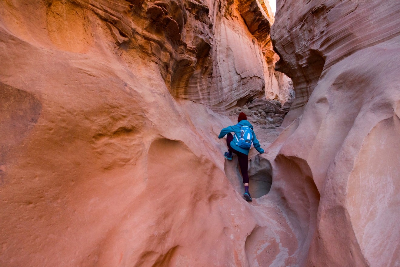 a hiker climbs through the sandstone formations of Escalante National Monument