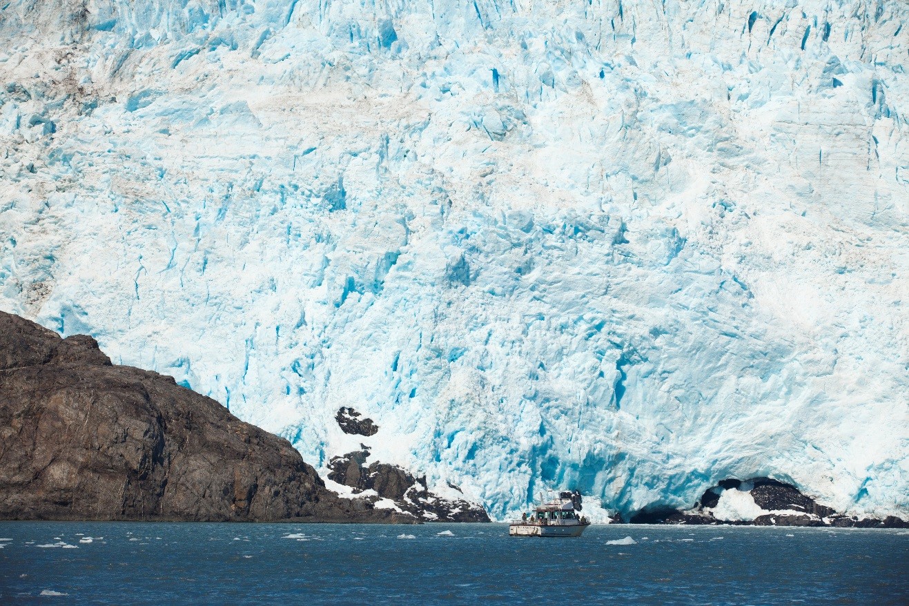a massive glacier dwarfs a small boat in Kenai National Park, Alaska