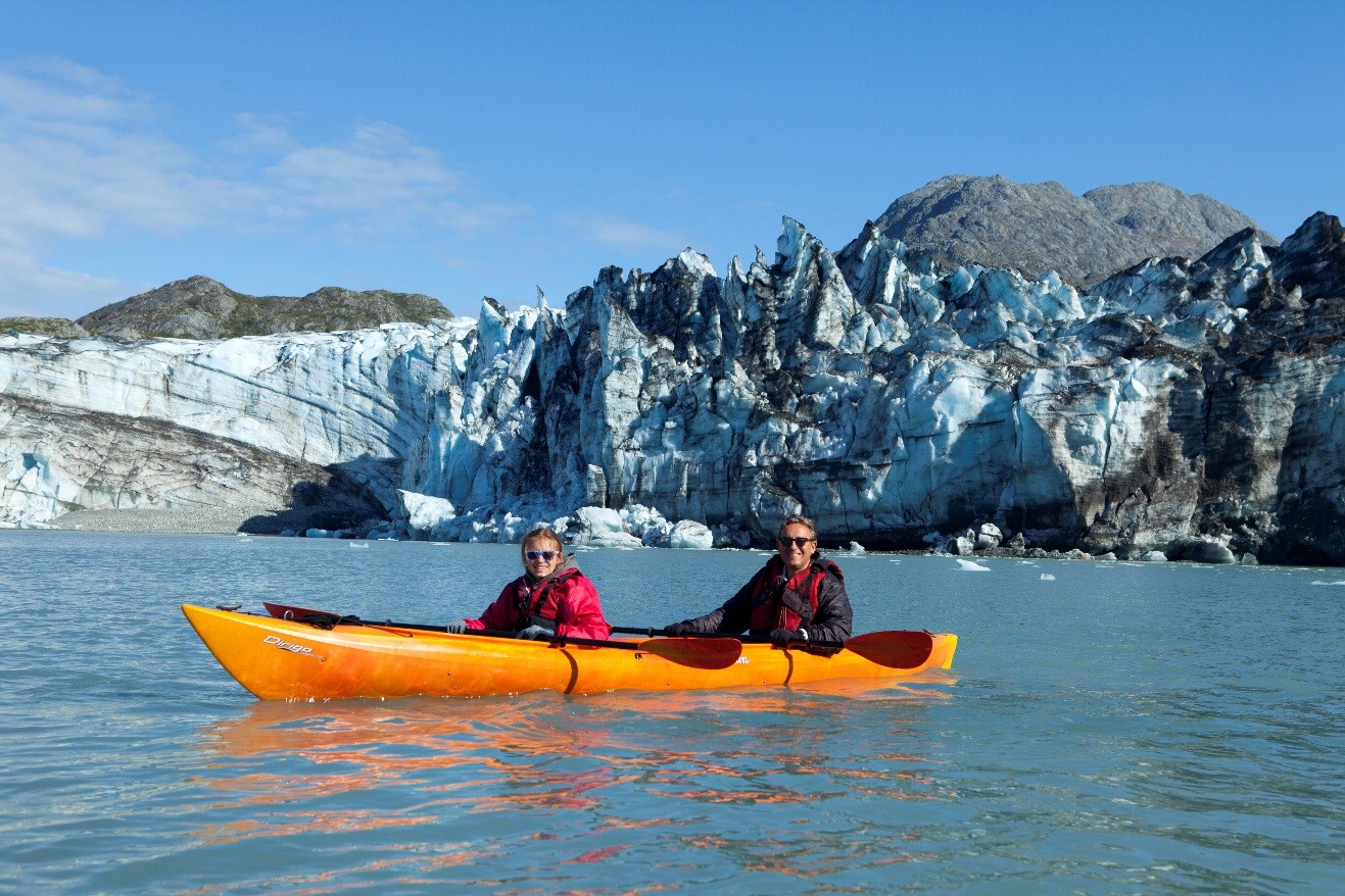 two kayakers sit in their boat in front of a glacier in Glacier Bay, Alaska