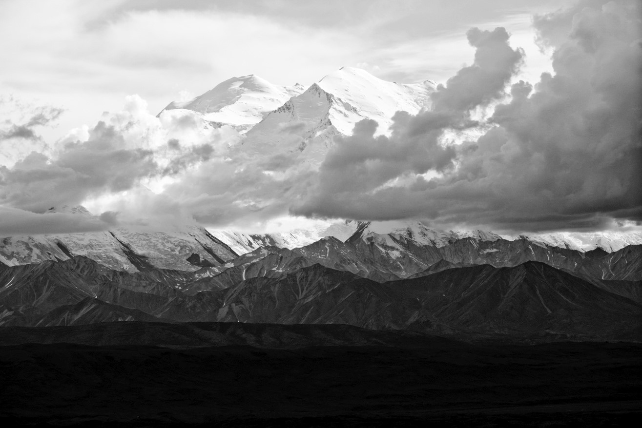 a black and white photograph of mount denali with clouds and ominous colors