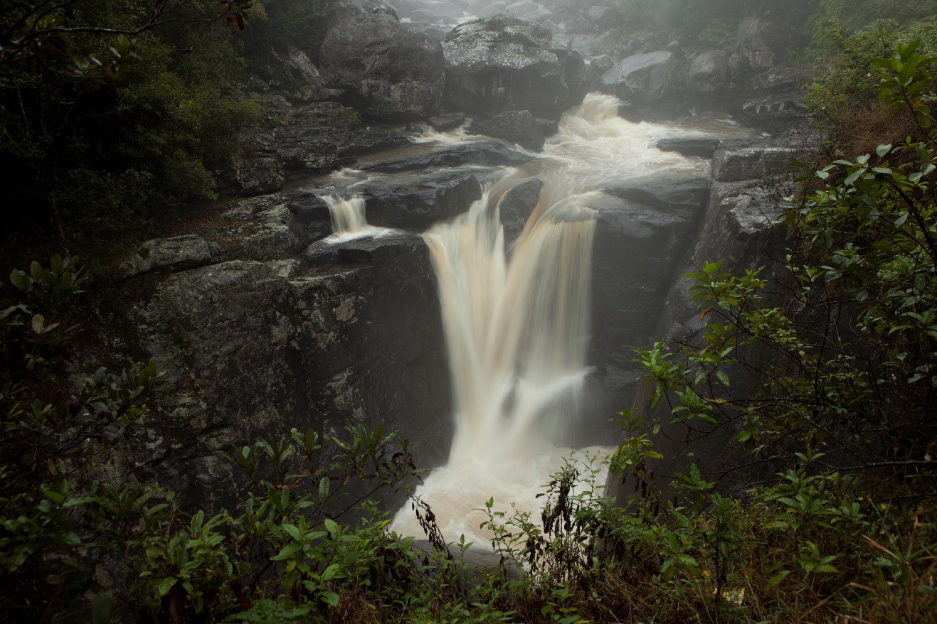 a waterfall pours down a slick rock face shrouded partially by mist in ranomafana national park, madagascar