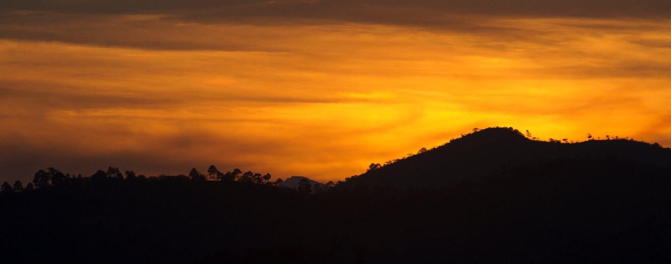 an orange sun sets below the mountains outside of Copan, Honduras