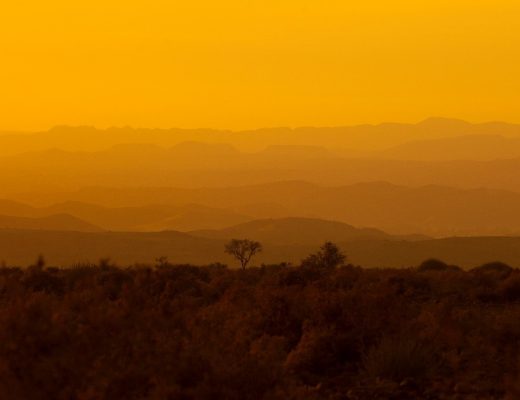a glowing orange sunset with layers of hills in the background in namibia