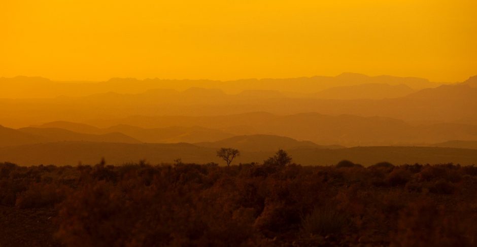 a glowing orange sunset with layers of hills in the background in namibia