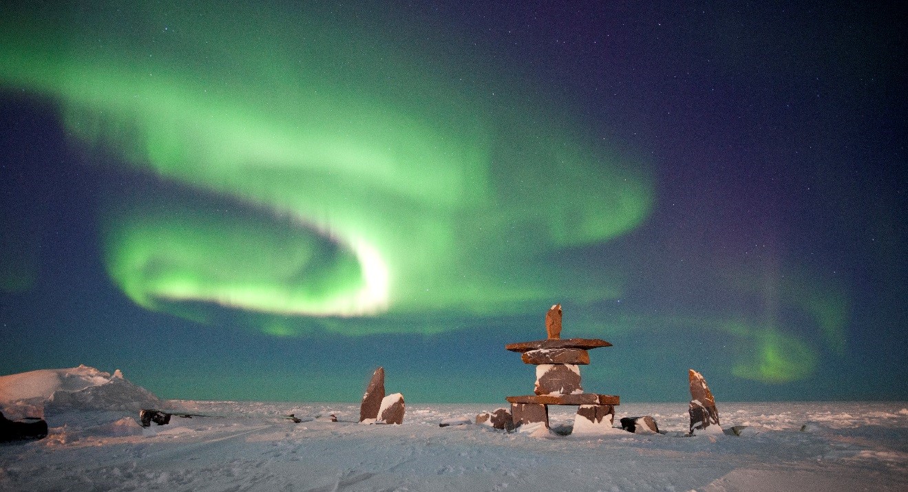 a vibrant display of the northern lights over churchill, canada with an inukshuk in the foreground