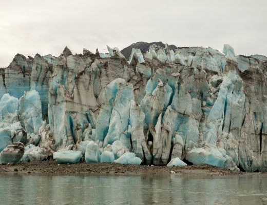 a jagged glacier comes closely to the water's edge in Alaska