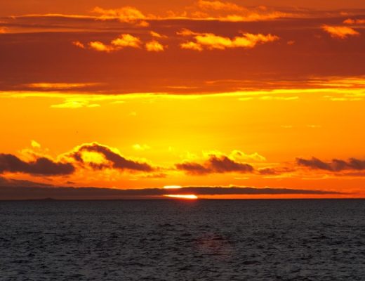 a bright orange and red sunset in the Galapagos over the horizon