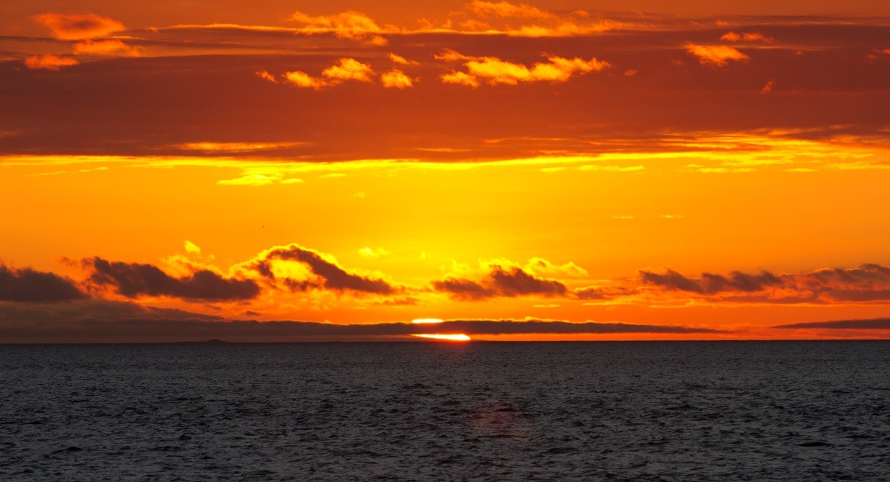 a bright orange and red sunset in the Galapagos over the horizon