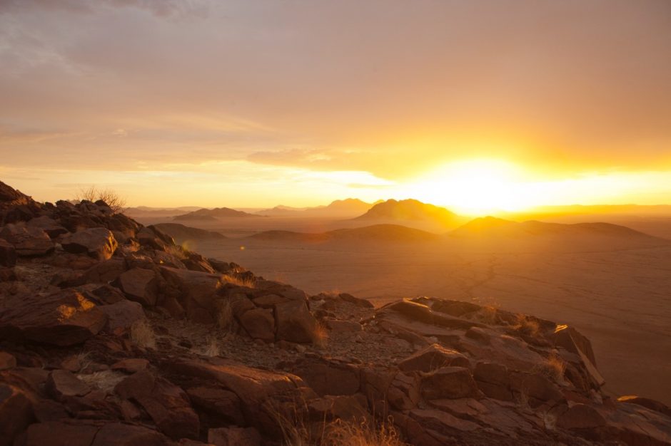 a spectacular sun set shines on the horizon of the namib desert