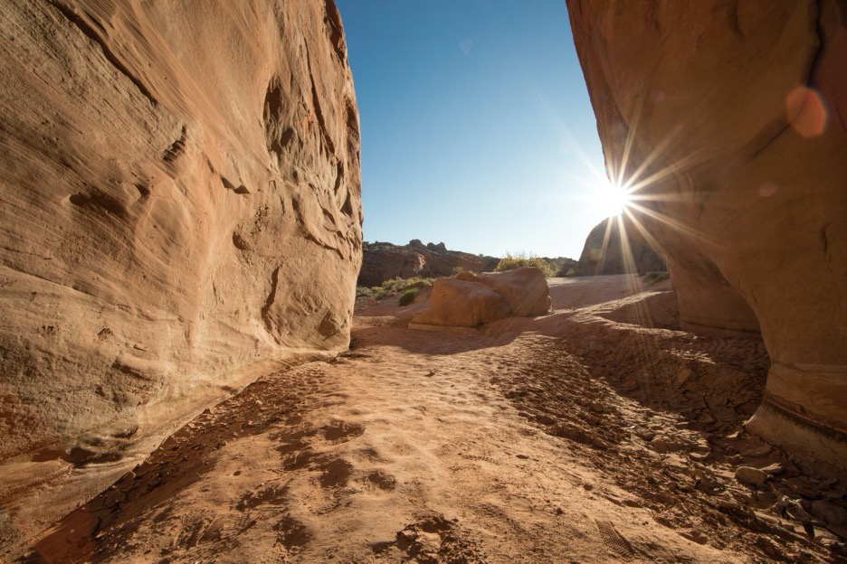 a sun rises in the desert viewed from within a slot canyon
