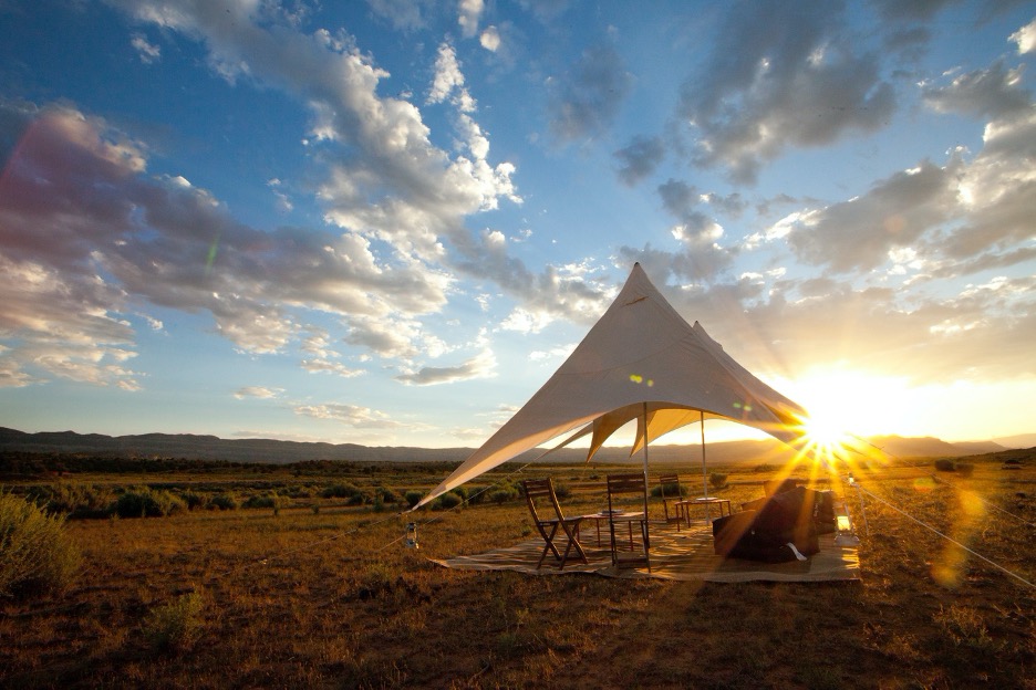 a canvas tent sits in the desert with sun setting