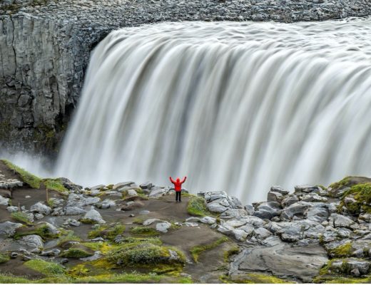 an adventurer stands in front of an amazing silky waterfall in iceland