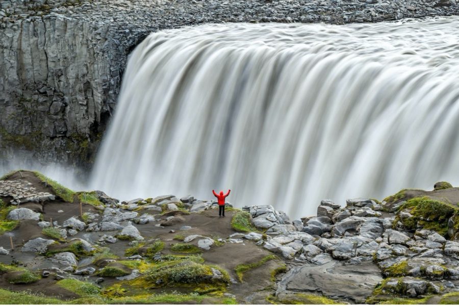 an adventurer stands in front of an amazing silky waterfall in iceland