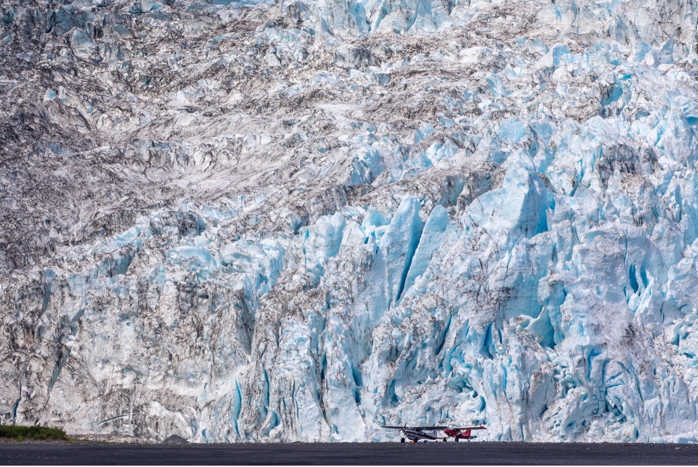 two planes site below a towering glacier