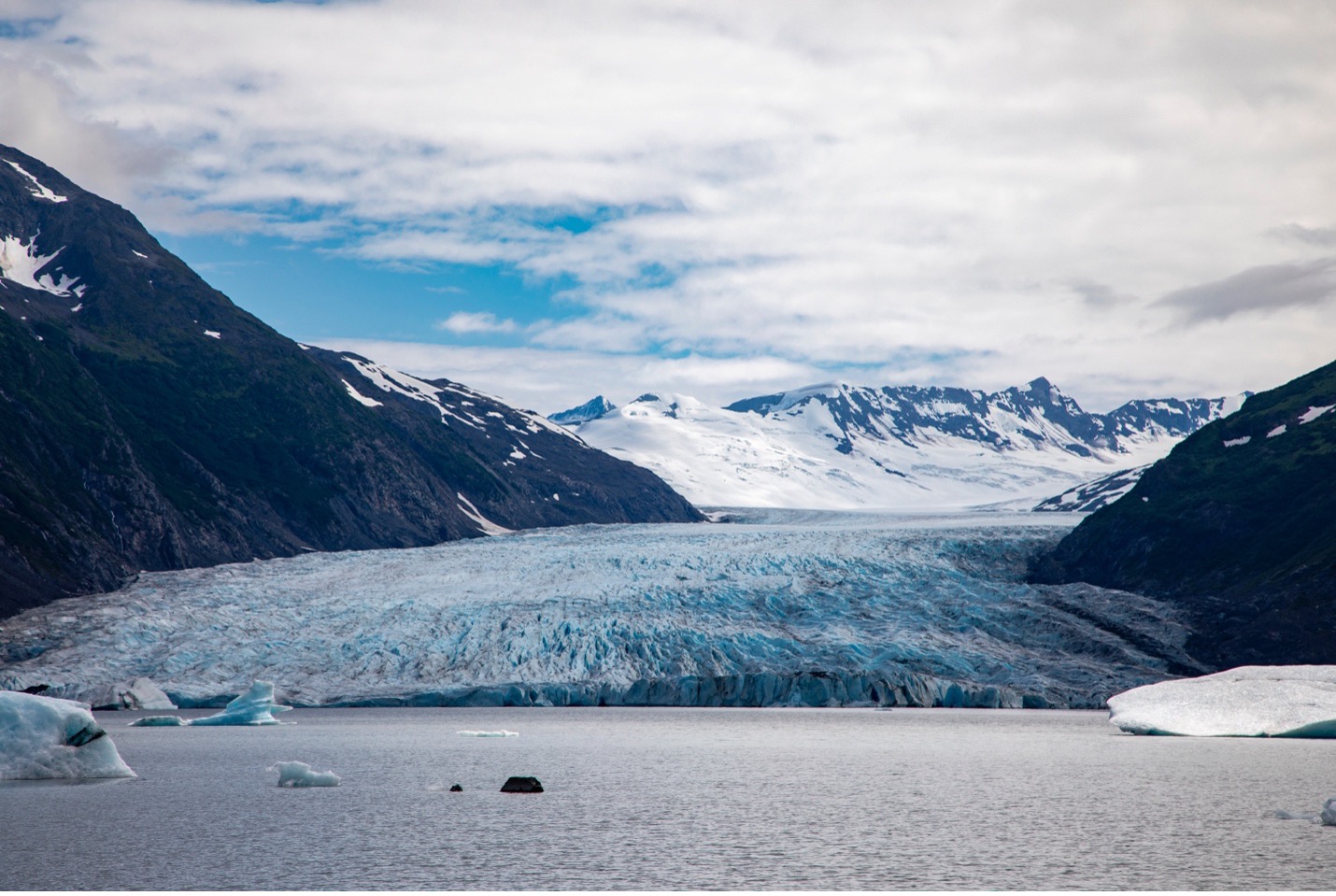 a wide shot of a glacier with some blue in the cloudy sky