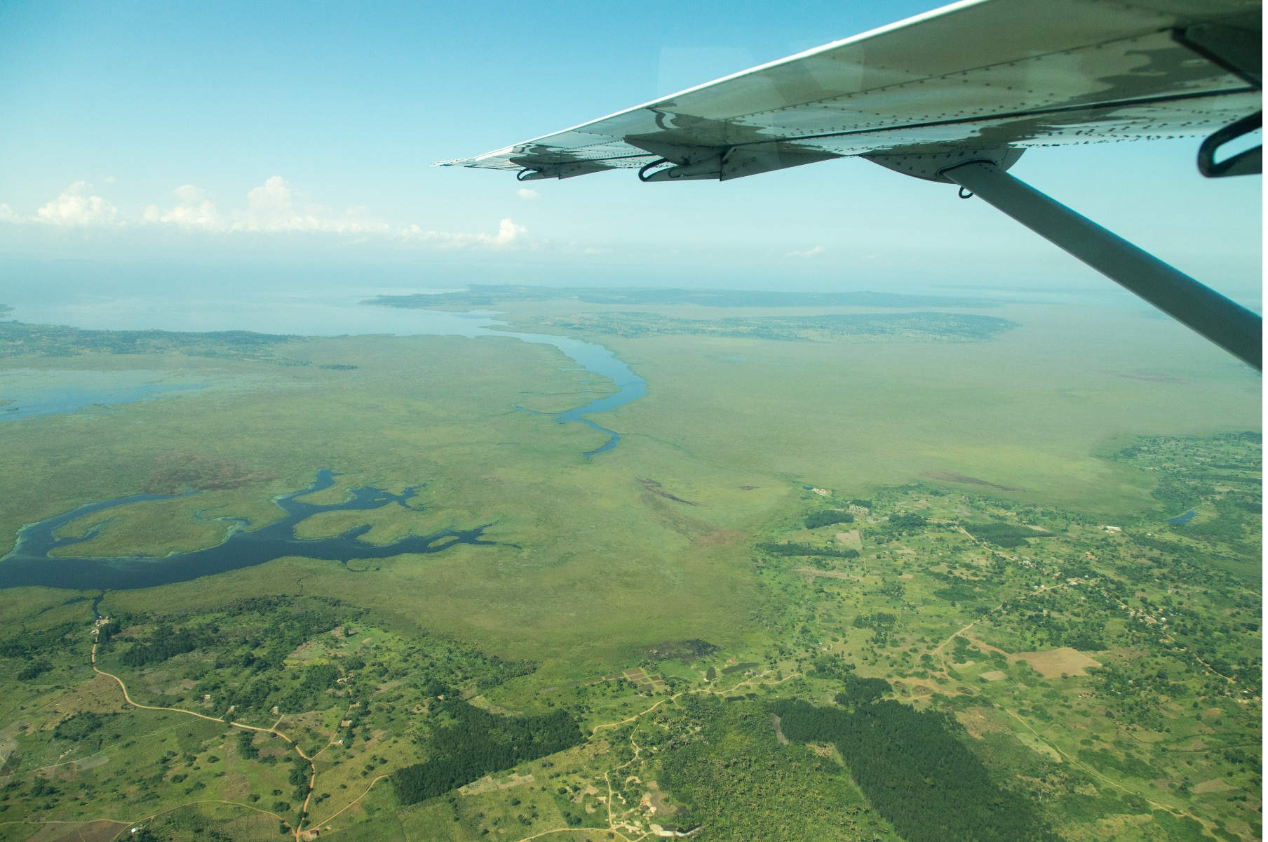 a photo is taken out of a small bushplane in Uganda with forest below