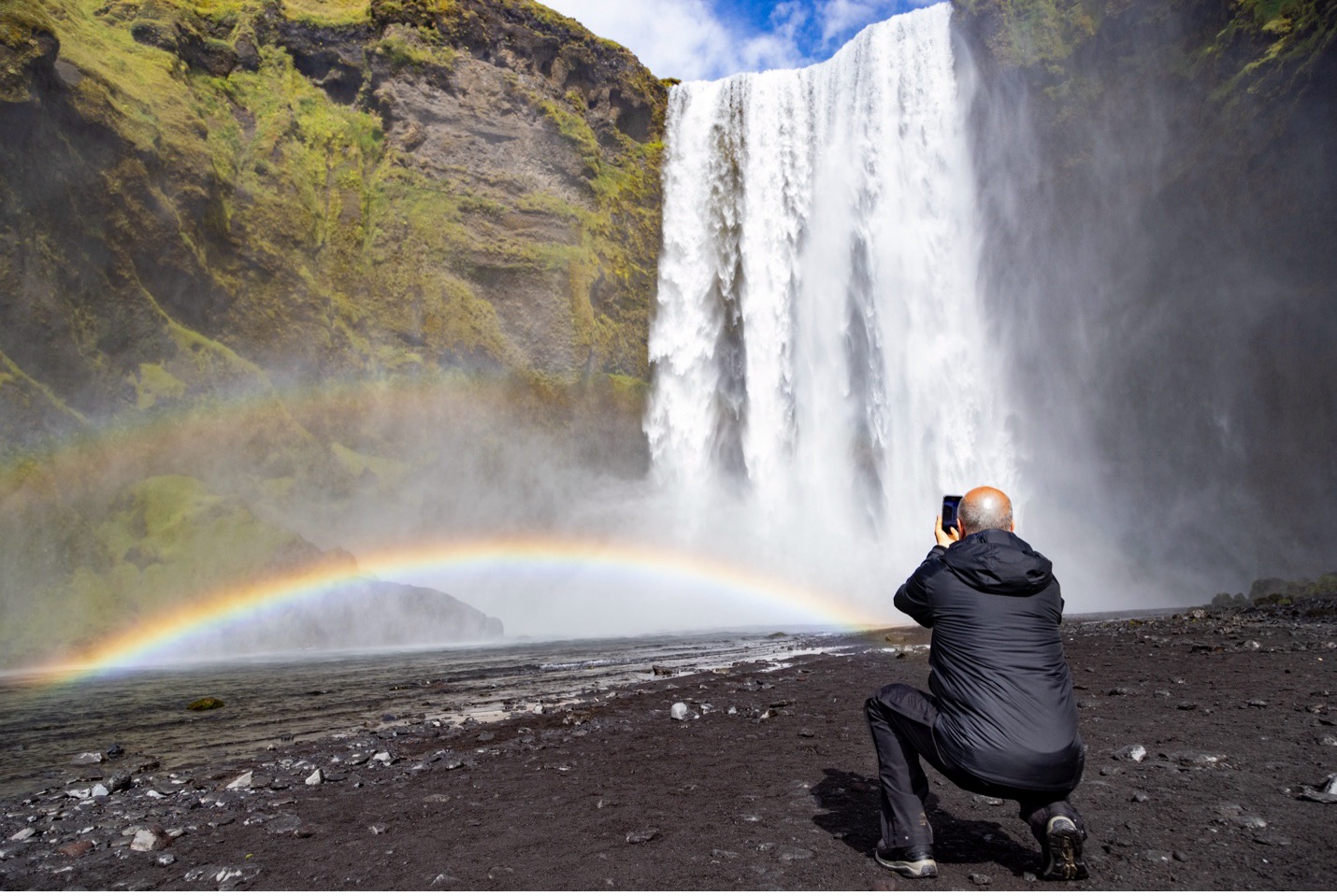 a man crouches to photograph a waterfall in iceland