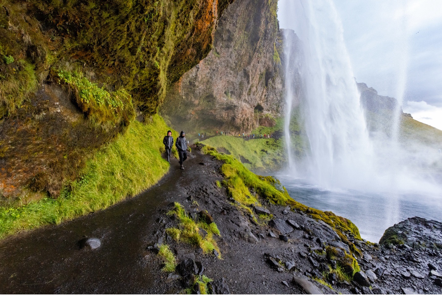 hikers walk around the back of a waterfall in iceland