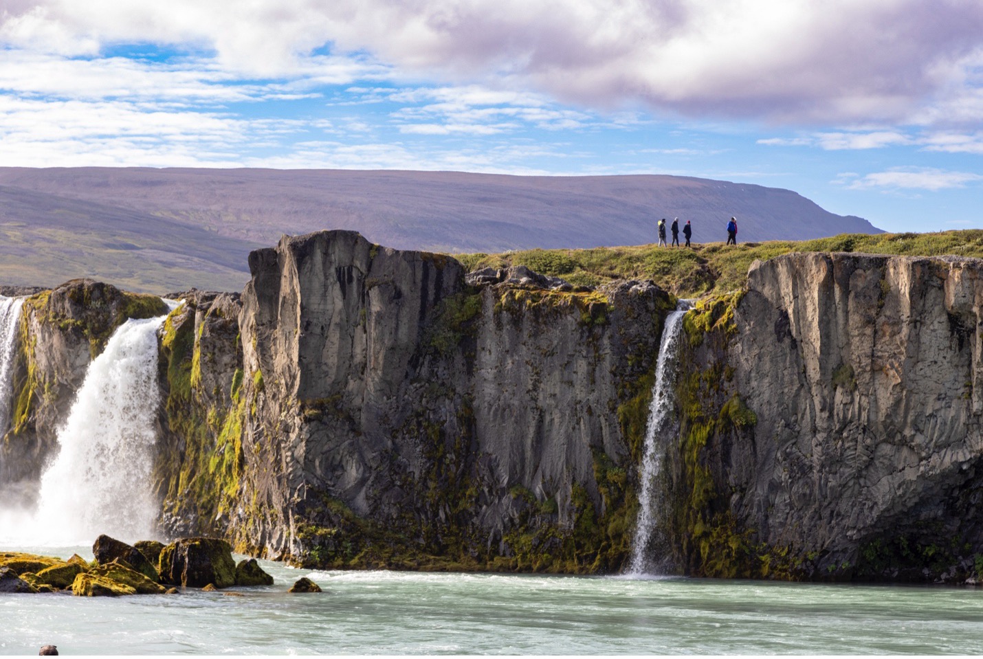 hikers walk a cliff on top of godafoss waterfall in iceland