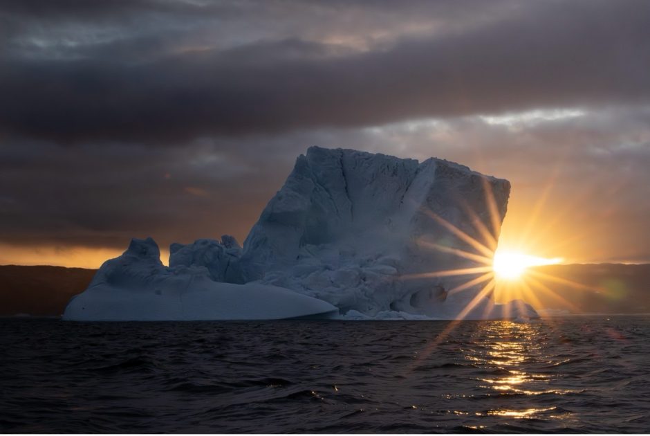 a large iceberg with sunburst on the horizon